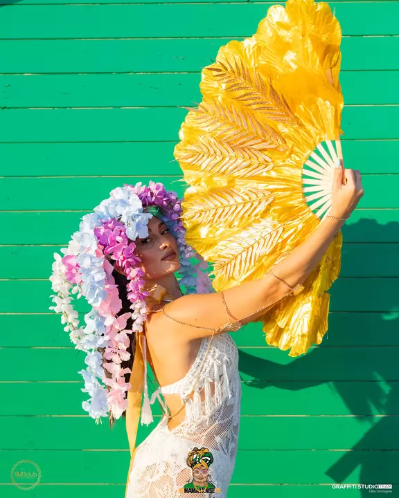 Performer con parrucca di fiori e grande ventaglio dorato su parete verde