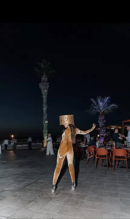 Performer in tuta di velluto dorato con copricapo a cilindro, sulla terrazza tra le palme