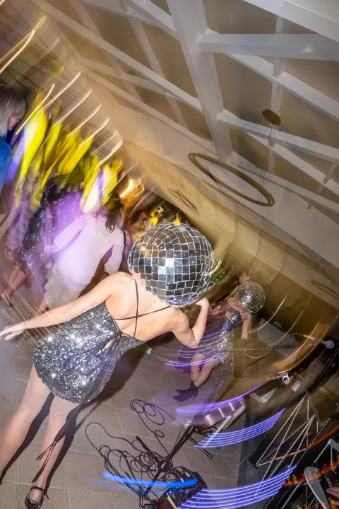 Performer con testa a palla specchiata e abito di paillettes, tra le luci colorate