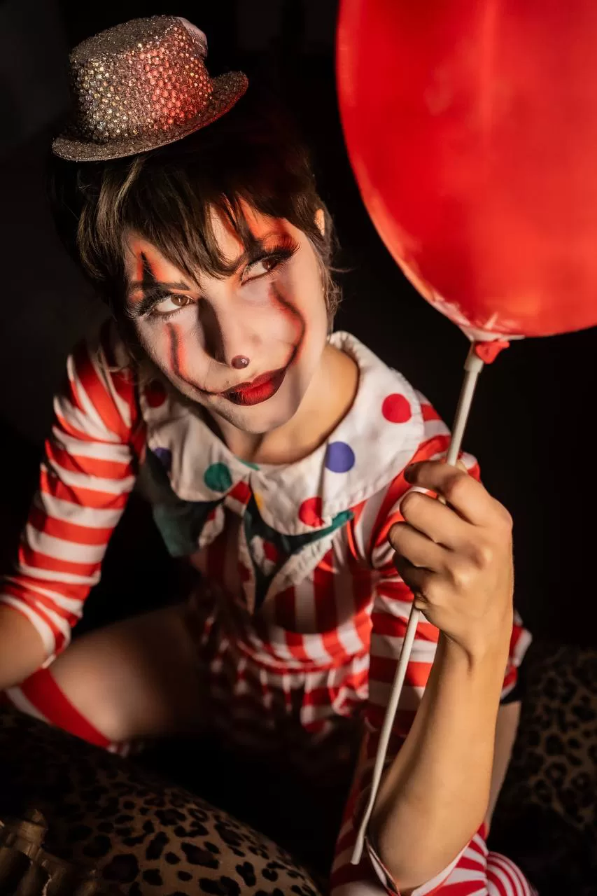 Performer truccata da clown con cappellino di strass e palloncino rosso, festa a tema Halloween
